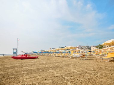 Cankurtaran kulesi, güneşli bir yaz sabahı sahilde bir cankurtaran botunun yanında arka planda İtalya 'nın Adriyatik kıyısında serinleyen banyocular var..