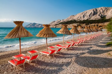 Sunshades and orange deck chairs on beach at Baska - Krk - Croat clipart
