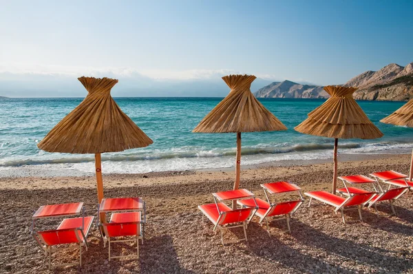 Parasoller och orange solstolar på stranden på baska - krk - kroatiska — Stockfoto