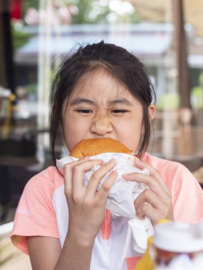 Asyalı küçük kız hamburger yiyor. Asyalı çocuklar tavuk peynirli hamburger yer.. 