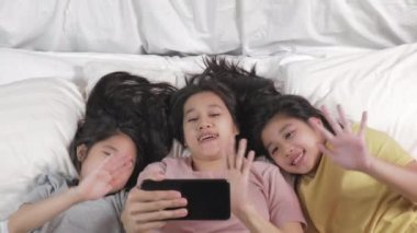 4K. Mutlu anne ve çocuğu yatakta babalarına selfie ya da video çekiyor. Aile kavramı anne ve kızı video aracılığıyla babayla bağlantı kuruyor..
