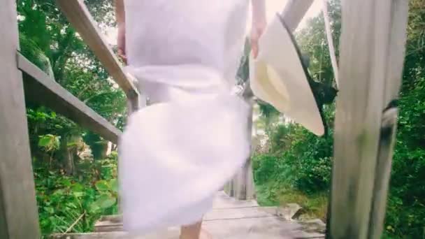 4K女はビーチへの木製の階段を歩く白いドレスを身に着けている 観光客の女性は 熱帯ビーチへの階段を歩くプーケットタイの夏休みの休暇のコンセプト — ストック動画