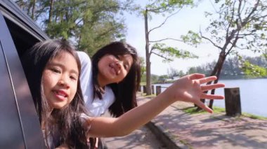 Ağır çekim Asyalı aile tatilde birlikte tatil yapıyor. Çocuklar arka koltukta oynamak için arabanın camını açarlar. Çocuklar gülen yüzle çok mutlu hissediyorlar..