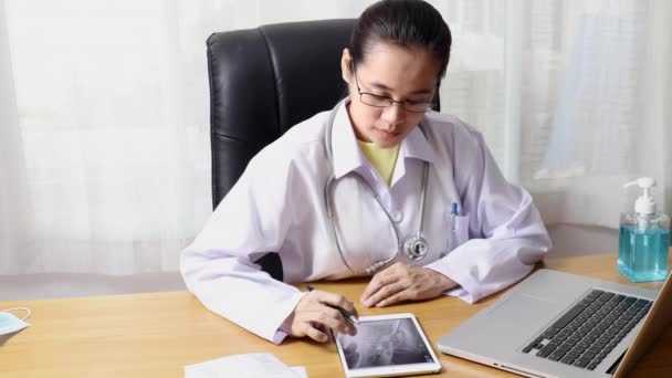 4K女医生戴着防护面罩 在平板电脑上看着X光 并在笔记本电脑上输入病人的报告 在诊所工作的医生 — 图库视频影像