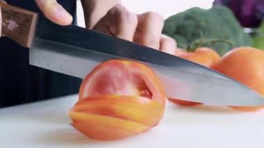 4K Kadın Eli Kesme Kurulu 'nda taze domates kesiyor. Dişi el, çiğ domatesi kesme tahtasındaki bıçakla daireler çiziyor. sağlıklı gıda konsepti.
