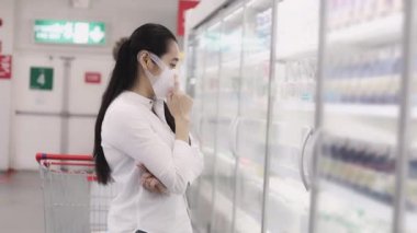Koruyucu maskeler takan Asyalı kadınlar süpermarketlerde alışveriş arabasını itip tutuyor. Kadın, yiyecek bir şeyler almak için bakkal arıyor. Covid-19 'dan sonra yeni normal. Aile kavramı.