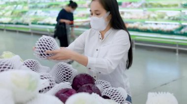 Süpermarkette koruyucu yüz maskesi takan Asyalı bir kadın. Kadın, yiyecek bir şeyler almak için bakkal arıyor. Covid-19 'dan sonra yeni normal. Aile kavramı. Kamera Hareketi Teknikleri.