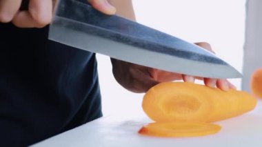 4K Kadın Eli kesme tahtasında taze havuç kesiyor. Dişi el çiğ havuçları kesme tahtasındaki bıçakla daireler halinde dilimliyor. sağlıklı gıda konsepti.