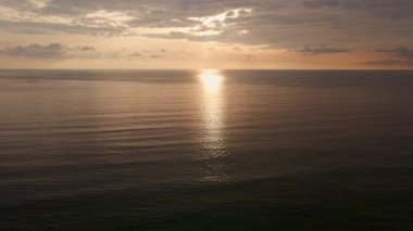 4K UHD hava görüntüsü İHA görüntüsü denizden yansıyan bulutlar, gün batımı ve güneş ışığı ile karaya çıkmak için denizin bir aşağı bir geri hareket ediyor. Deniz aşırı güzel gün batımı