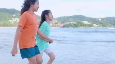 Asyalı mutlu aile akşamları sahilde tatilin tadını çıkarır. Anne ve çocuk plajda birlikte oynarken rahatlar. Anne ve kızı yaz tatili seyahati konsepti. Kamera Hareketi Teknikleri.