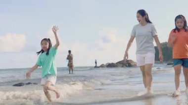 Asyalı mutlu aile akşamları sahilde tatilin tadını çıkarır. Anne ve çocuk plajda birlikte oynarken rahatlar. Anne ve kızı yaz tatili seyahati konsepti. Kamera Hareketi Teknikleri.