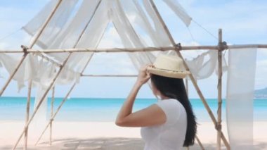 Gezgin kadının 4K portresi halk plajında tıbbi maske kullanıyor. Genç Asyalı kadın koruyucu maskesiyle plaj tatillerinin tadını çıkarıyor. Covid-19 yaz tatili