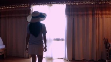 4K kamera hareket ediyor, arkadan bakıyor, valiz açan, dantelli mutlu seyahat eden kadınlar lüks villa otelinde dikiliyor ve pencereden tropikal deniz manzarasının keyfini çıkarıyorlar. Tatil seyahati