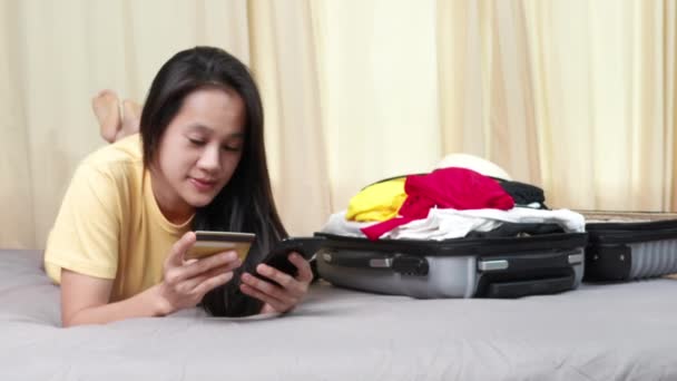 Asyalı Mutlu Kadın Evdeki Yatakta Cep Telefonu Kredi Kartıyla Seyahat — Stok video