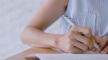 Kapalı kapılar ardında kadınlar kalem kâğıdı kullanır. Kadın eli, beyaz bir çarşafta mavi bir kalemle yazıyı kapatıyor. Kadın bir kağıt parçasına bilgi yazıyor..