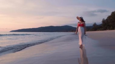 Güzel kadınların yavaş çekimde yürüdükleri beyaz elbiseler giyerler ve gün batımının tadını çıkarırlar. Günbatımı gökyüzü ile tropik plajda yürüyen turist kadınlar. Özgürlük cenneti tatil tatili yaz konsepti