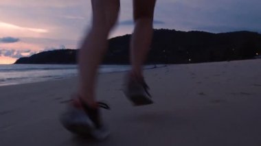 Bacak çalıştıran kadınlar spor ayakkabı giyerler gün batımında plajda koşmaya başlarlar. Koşan kadınlar sahilde koşuyor. Sabah plajda koşan kadın egzersizi..