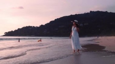 Güzel kadınların yavaş çekimde yürüdükleri beyaz elbiseler giyerler ve gün batımının tadını çıkarırlar. Günbatımı gökyüzü ile tropik plajda yürüyen turist kadınlar. Özgürlük cenneti tatil tatili yaz konsepti