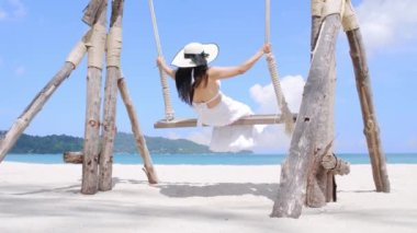 Özgürlüğün tadını çıkaran genç kadınların arkası sahilin yakınındaki salıncaklarda tek başlarına sallandıklarını hissediyor. Turist kadınlar tropik plajlarda salıncaktan hoşlanırlar. Phuket, Tayland. Yaz tatili konsepti.