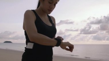 Kadın elleri ayarlıyor ya da akıllı saati kardiyo antrenman moduna ayarlıyor. Spor bilezikli bir kadın plajda koşmaktan keyif alıyor. Modern teknolojiyi kullanıyor..