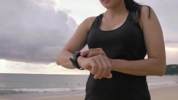 女子手调校或设置智能手表到有氧训练模式 拥有健身手镯的女性在海滩上享受户外运动时使用的是现代技术 — 图库视频影像
