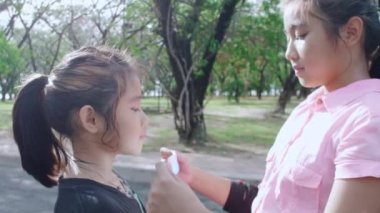 Asyalı abla covid-19 'u önlemek için parktaki kız kardeşine koruyucu yüz maskesi takmaya yardım ediyor. Salgın sırasında parkta oynamadan önce kız kardeşi için yüz maskesi takmış.