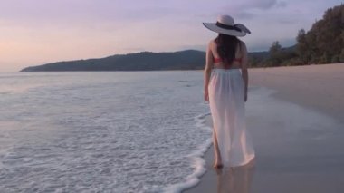 Güzel kadınların yavaş çekimde yürüdükleri beyaz elbiseler giyerler ve gün batımının tadını çıkarırlar. Günbatımı gökyüzü ile tropik plajda yürüyen turist kadınlar. Özgürlük cenneti tatil tatili yaz konsepti