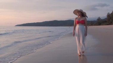 Güzel kadınların yavaş çekimde yürüdükleri beyaz elbiseler giyerler ve gün batımının tadını çıkarırlar. Günbatımı gökyüzü ile tropik plajda yürüyen turist kadınlar. Özgürlük cenneti tatil tatili yaz konsepti