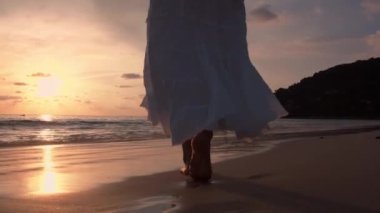 Altın gün batımında sahilde çıplak ayakla yürüyen bir kadın. Kumda ayak izleri bırakıyor. Yaz tatilindeki kadın turistler Tayland, Phuket plajında dinleniyor.. 