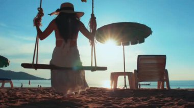 Özgürlüğün tadını çıkaran siluet görünümlü genç kadınlar gün batımına yakın salıncaklarda sallandıklarını hissediyorlar. Turist kadınlar tropik cennet sahillerinde salıncaktan hoşlanırlar. Phuket, Tayland.