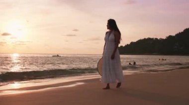 Güzel kadınların yavaş çekimde yürüdükleri beyaz elbiseler giyerler ve gün batımının tadını çıkarırlar. Günbatımı gökyüzü ile tropik plajda yürüyen turist kadınlar. Özgürlük cenneti tatil tatili yaz konsepti