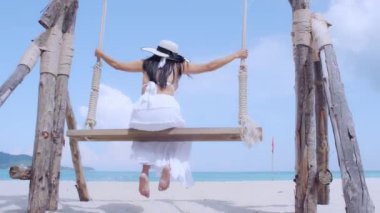 Özgürlüğün tadını çıkaran genç kadınların arka planda salıncaklarda sallandıklarını hissediyorum. Sahilde yalnız başlarına. Turist kadınlar tropik plajlarda salıncaktan hoşlanırlar. Phuket, Tayland. Yaz tatili konsepti.