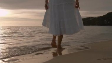 Altın gün batımında sahilde çıplak ayakla yürüyen bir kadın. Kumda ayak izleri bırakıyor. Yaz tatilindeki kadın turistler Tayland, Phuket plajında dinleniyor.. 