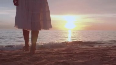 Altın gün batımında sahilde çıplak ayakla yürüyen bir kadın. Kumda ayak izleri bırakıyor. Yaz tatilindeki kadın turistler Tayland, Phuket plajında dinleniyor.. 