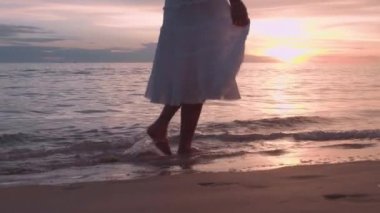 Altın gün batımında sahilde çıplak ayakla yürüyen bir kadın. Kumda ayak izleri bırakıyor. Yaz tatilindeki kadın turistler Tayland, Phuket plajında dinleniyor.. 