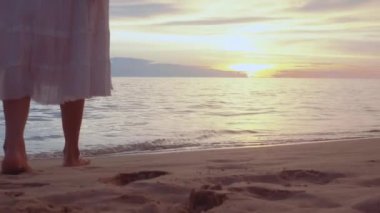 Altın gün batımında sahilde çıplak ayakla yürüyen bir kadın. Kumda ayak izleri bırakıyor. Yaz tatilindeki kadın turistler Tayland, Phuket plajında dinleniyor.. 