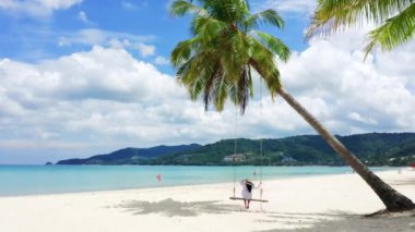 4K Phuket, Tayland. Plaj cenneti ve beyaz gömlekli kız. Kadınlar salıncakta sallanır, hindistan cevizi palmiyesinin altında, güzel tropik sahilde, beyaz kumsalda..