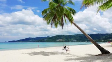 4K Phuket, Tayland. Plaj cenneti ve beyaz gömlekli kız. Kadınlar salıncakta sallanır, hindistan cevizi palmiyesinin altında, güzel tropik sahilde, beyaz kumsalda..