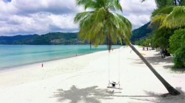 4K Phuket, Tayland. Plaj cenneti ve beyaz gömlekli kız. Kadınlar salıncakta sallanır, hindistan cevizi palmiyesinin altında, güzel tropik sahilde, beyaz kumsalda..