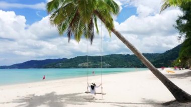 4K Phuket, Tayland. Plaj cenneti ve beyaz gömlekli kız. Kadınlar salıncakta sallanır, hindistan cevizi palmiyesinin altında, güzel tropik sahilde, beyaz kumsalda..