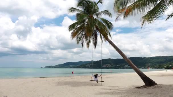 タイの4Kプーケット 白いシャツの女の子とビーチスイングと熱帯のビーチの楽園 女性は美しい熱帯のビーチでヤシの木の下でスイングでリラックス白い砂 — ストック動画