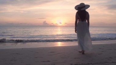 Altın gün batımında, plajda çıplak ayakla yürüyen 4K Slow motion kadın. Kumda ayak izleri bırakıyor. Yaz tatilindeki kadın turist. Tayland, Phuket plajında dinleniyor.. 