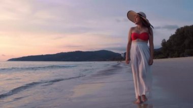 Altın gün batımında, plajda çıplak ayakla yürüyen 4K Slow motion kadın. Kumda ayak izleri bırakıyor. Yaz tatilindeki kadın turist. Tayland, Phuket plajında dinleniyor.. 