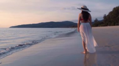 Altın gün batımında, plajda çıplak ayakla yürüyen 4K Slow motion kadın. Kumda ayak izleri bırakıyor. Yaz tatilindeki kadın turist. Tayland, Phuket plajında dinleniyor.. 