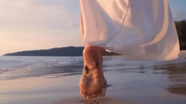 Altın gün batımında, plajda çıplak ayakla yürüyen 4K Slow motion kadın. Kumda ayak izleri bırakıyor. Yaz tatilindeki kadın turist. Tayland, Phuket plajında dinleniyor.. 