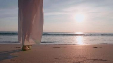 Altın gün batımında, plajda çıplak ayakla yürüyen 4K Slow motion kadın. Kumda ayak izleri bırakıyor. Yaz tatilindeki kadın turist. Tayland, Phuket plajında dinleniyor.. 