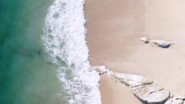 4K hava aracı yukarıdan aşağıya kuş bakışı deniz mavi dalgaları kaya ve kumda kırılıyor. Deniz suyunun güzel dalgaları sahile gelir.
