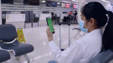 4K Asyalı turist kadınlar salgın koronavirüs salgını için koruyucu yüz maskeleri takarlar. Sosyal mesafeli kürsüye otururlar. Arkadaş veya aileyle iletişim kurmak için akıllı telefon kullanırlar. Kadınlar yeşil ekranlı cep telefonu kullanırlar.