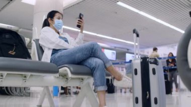 4K Asyalı turist kadınlar salgın koronavirüs salgını için koruyucu yüz maskeleri takarlar. Sosyal mesafeli kürsüye otururlar. Arkadaş veya aileyle iletişim kurmak için akıllı telefon kullanırlar. Kadınlar yeşil ekranlı cep telefonu kullanırlar.