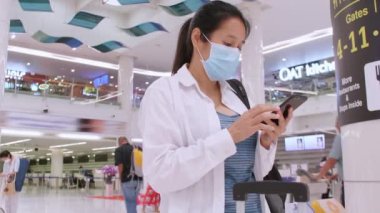 4K Asyalı turist kadınlar salgın koronavirüs salgını için koruyucu yüz maskeleri takarlar. Sosyal mesafeli kürsüye otururlar. Arkadaş veya aileyle iletişim kurmak için akıllı telefon kullanırlar. Kadınlar yeşil ekranlı cep telefonu kullanırlar.